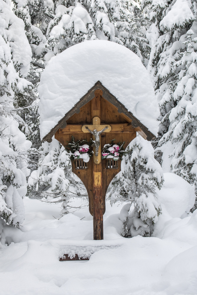Ein Holzkreuz im Wald mit viel Schnee bedeckt